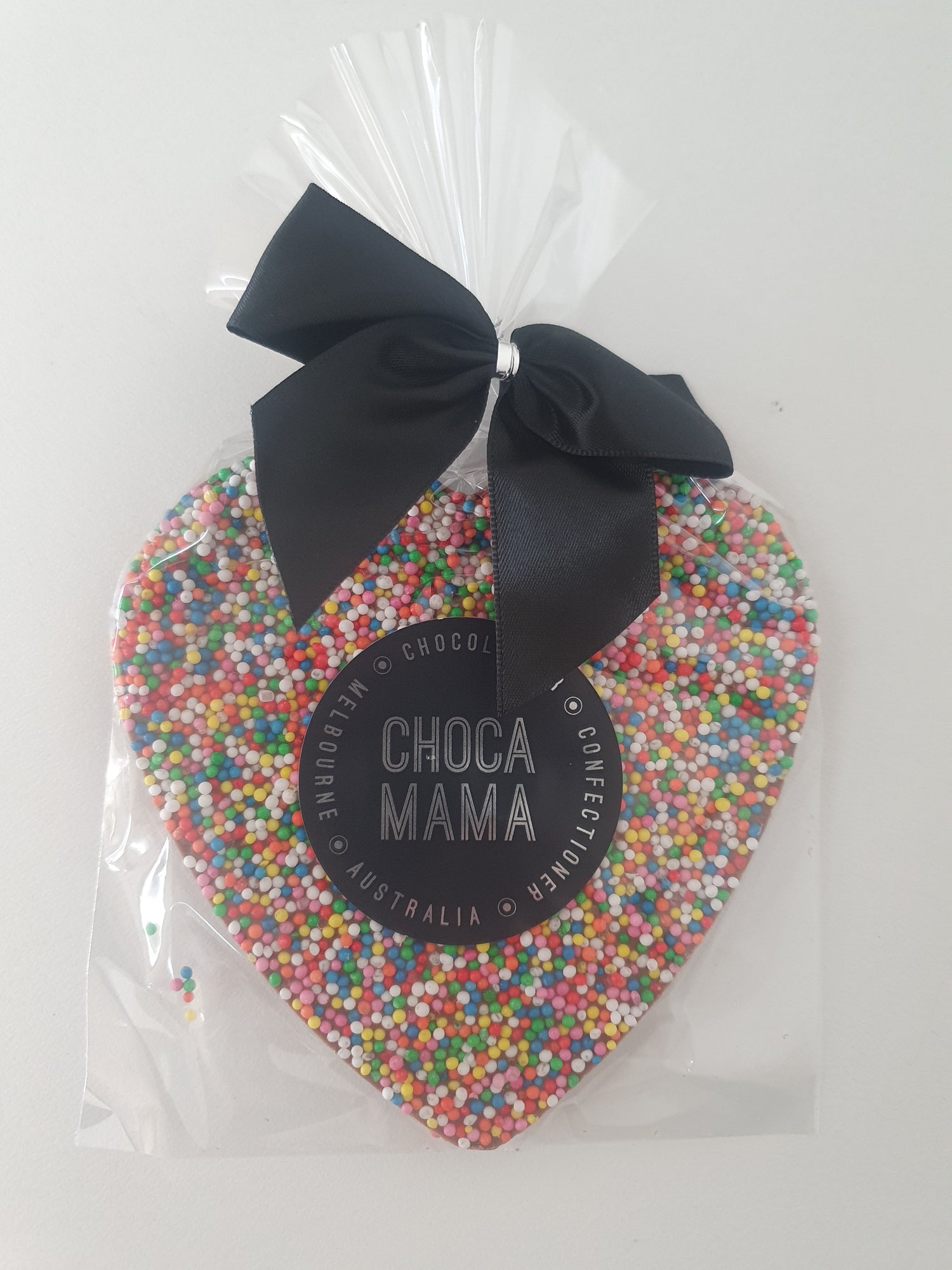 Packaged chocolate heart with colorful sprinkles and a black bow, branded 'Choco Mama'.