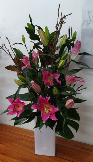 Large arrangement of pink oriental lilies in a tall white ceramic container.